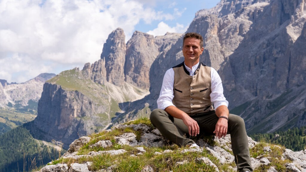Alexander Rier beim CD-Cover-Shooting in der Steinernen Stadt am Sellajoch, sitzend in Trachtenweste vor der Bergkulisse